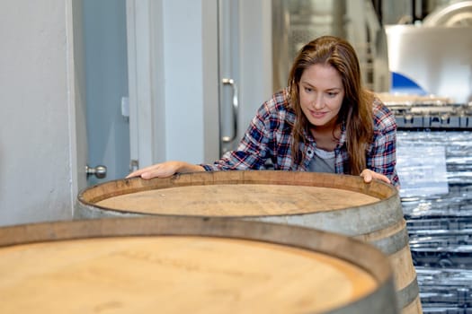 Winery worker woman stand near wine fermentation tank and check the product in modern factory.