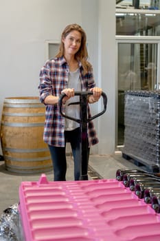 Winery worker woman hold hand of factory truck to carry the containers of wine bottle.