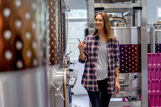 Winery worker woman walk and check the process of the machine in the modern factory with happiness.