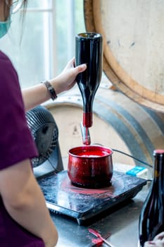 Winery worker hold the wine bottle to dip the bottleneck into wax in the process of seal cap in the factory.