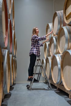 Vertical image of winery worker woman stand on the stairs to check the product in modern factory.