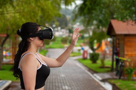 young girl in a park wearing augmented reality glasses with her hand raised touching a reality that does not exist. High quality photo