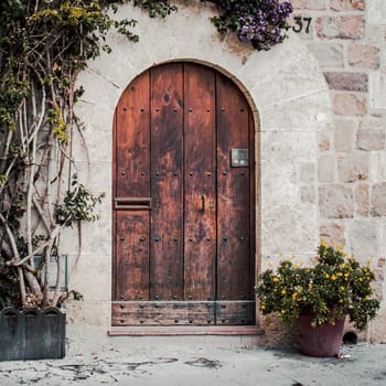 Brown wooden old door made from slats photo. Grey brick house surrounded by green tree foliage. Street sign number 3. Entrance with keyhole and mail slot. High quality picture for wallpaper, article