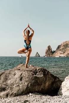 Yoga on the beach. A happy woman meditating in a yoga pose on the beach, surrounded by the ocean and rock mountains, promoting a healthy lifestyle outdoors in nature, and inspiring fitness concept