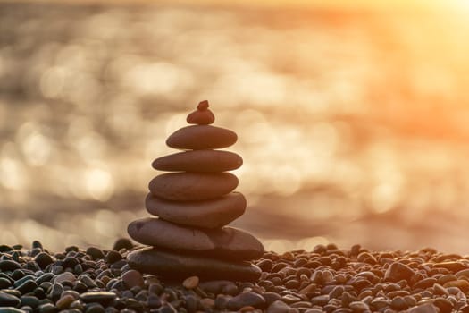 Balanced rock pyramid on pebbles beach. Golden sea bokeh on background. Selective focus, zen stones on sea beach, meditation, spa, harmony, calm, balance concept