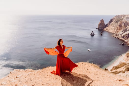 Woman red dress sea., posing on a rocky outcrop high above the sea. Girl on the nature on blue sky background. Fashion photo