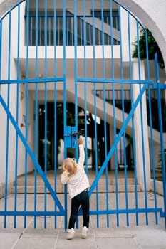 Little girl reaches for the lock on the metal arched gate of the house. Back view. High quality photo