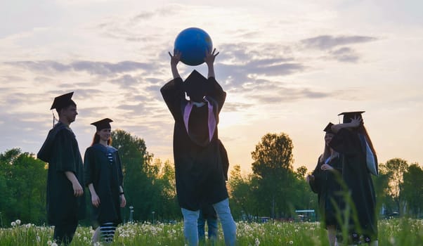 Graduates in costume playing with a ball at sunset