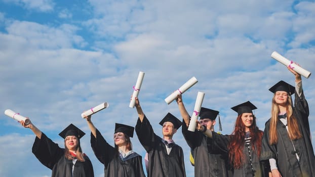 Cheerful graduates pose with raised diplomas on a sunny day