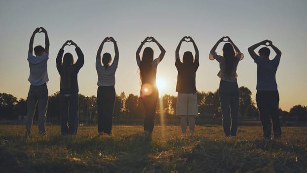 Seven friends make a heart shape from their hands at sunset