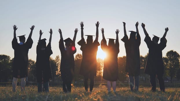 College graduates in robes waving at sunset