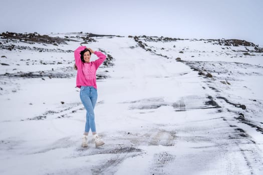 Woman in pink sweater posing on a snowy road in Iceland