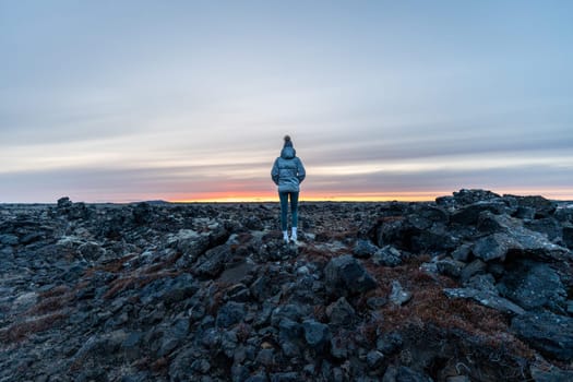 Woman posing in an ancient lava field watching sunset