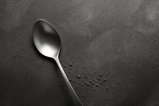 A spoon with scattered grains on a dark textured background. Minimalistic kitchen concept.