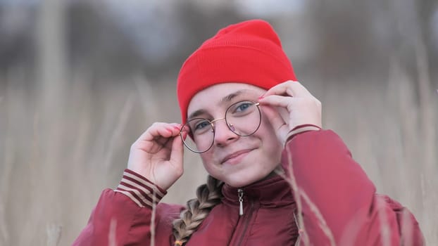 Portrait of a teenage girl in glasses standing in tall grass in the fall