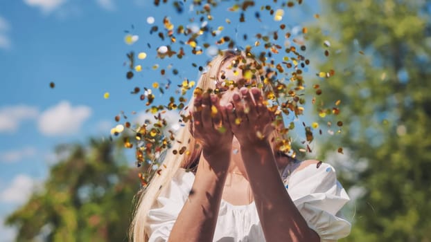 The girl blows a golden confetti out of her hands