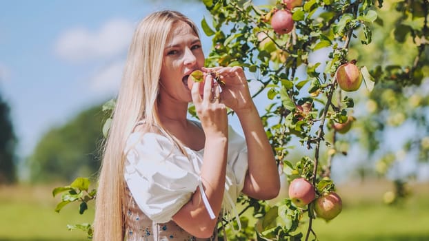 A young woman plucks an apple from a tree and eats it