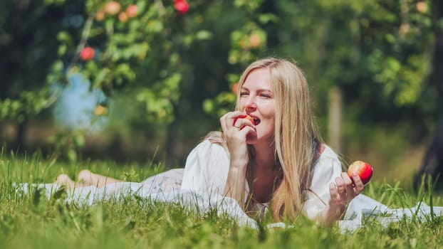 A young woman is lying on the grass in the garden eating an apple