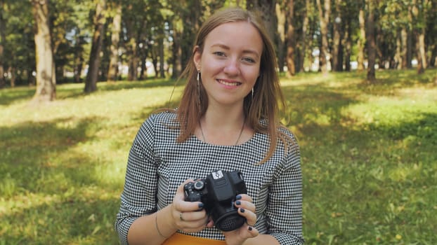 A young girl photographer with a camera poses in the park