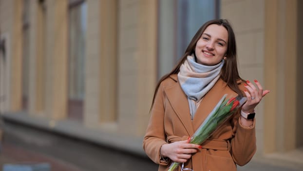Portrait of a happy brunette girl with a tulip in the background of the city in the cold season