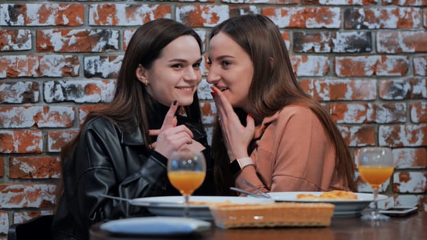 Two young girls gossiping sitting in a cafe