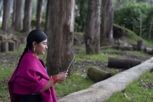 copyspace of a young indigenous girl from otavalo, ecuador sitting on a log in a forest, connecting to the internet with a tablet. High quality photo