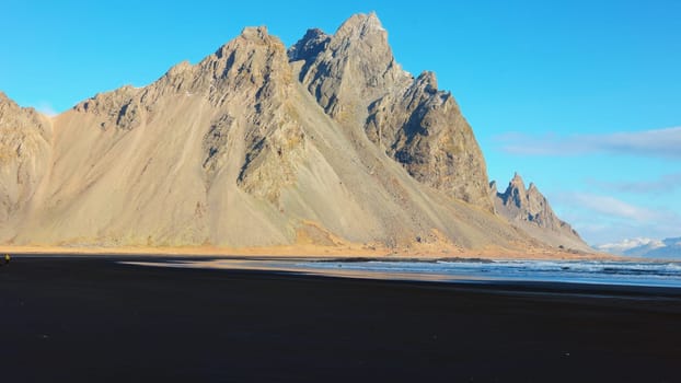 Vestrahorn mountains on arctic peninsula with natural black sand beach and beautiful skyline, sightseeing adventure. Ocean coastline shore and hills forming majestic landscape. Handheld shot.