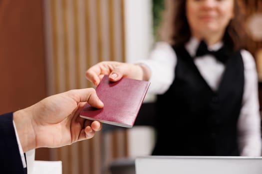 Businessman providing passport for check in process, giving identification documents to receptionist at front desk. Adult arriving at hotel for registration, id papers in lobby. Close up.