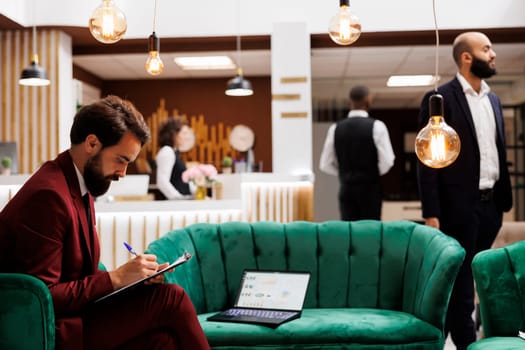 Entrepreneur taking notes on files at hotel, using lapotp to review international conference speech before meeting with executive board. Employee travelling on business trip for development.