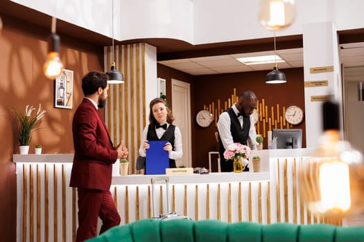 Hotel concierge greet client at reception, providing luxury accommodation services. Businessman finishes check in process, marking the beginning of business trip and preparing for productive stay.