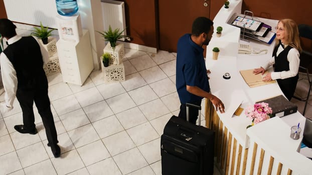 Hotel guest entering at reception lobby, preparing to register and start exotic seaside holiday. Summer resort employees team providing luxury service for travellers. Handheld shot.