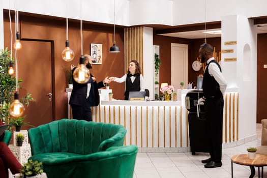 Hotel staff gives access key card to businessman travelling for work, doing check in and preparing for meeting. Entrepreneur in suit talking to front desk receptionist in lobby.