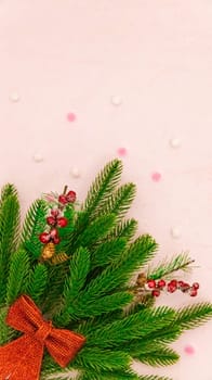 A bouquet of fir branches with a red bow and fluffy balls of snow lie on the left on a soft pink background with a copy of the space on top, a flat lay close-up.