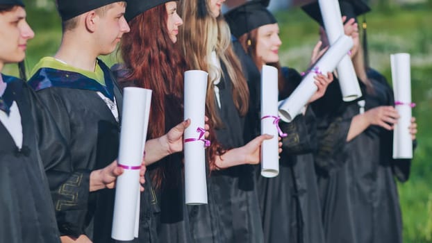 Scrolls of diplomas in the hands of a group of graduates