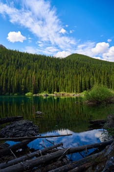 Incredibly beautiful transparent emerald calm lake with reflection of rocky mountain on the Black Prince Cirque Trail. An old dry coniferous tree fell in a mountain forest on the shore of a lake