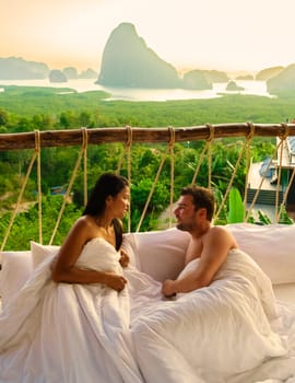 A couple in an outdoor bedroom watching the sunrise over Sametnangshe mountains in Phangnga Bay with mangrove forest in the Andaman Sea Phangnga, Thailand