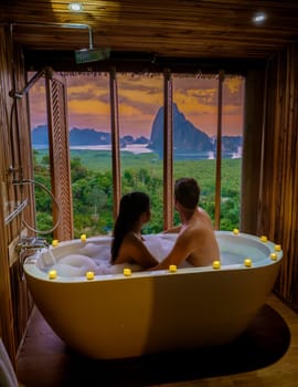 A couple of men and woman in a bathtub looking at the sunset over Sametnangshe viewpoint mountains in Phangnga Bay with mangrove forest in the Andaman Sea in Phangnga, Thailand, a couple in bathtub