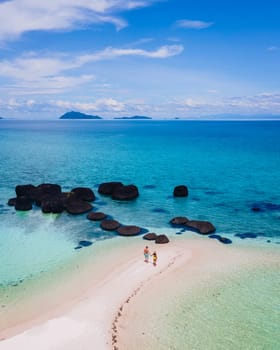 couple walking at the beach of Koh Kham Trat Thailand, aerial view of the tropical island near Koh Mak Thailand. white sandy beach with palm trees and big black boulder stones in the ocean