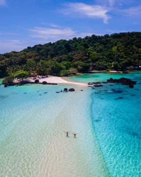 couple walking at the beach of Koh Kham Trat Thailand, aerial view of the tropical island near Koh Mak Thailand. white sandy beach with palm trees and big black boulder stones in the ocean of Koh Kham