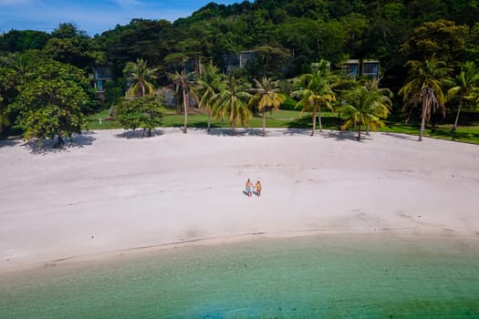 couple walking at the beach of Koh Kham Trat Thailand, aerial view of the tropical island near Koh Mak Thailand with a white sandy beach with palm trees and big black boulder stones in the ocean
