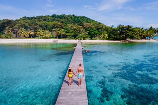 couple walking at a wooden pier in the ocean of Koh Kham Trat Thailand, aerial view of the tropical island near Koh Mak Thailand. white sandy beach with palm trees and big black boulder stones