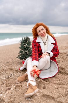 Lady in plaid shirt holding a gift in his hands enjoys beach with Christmas tree. Coastal area. Christmas, New Year holidays concep.