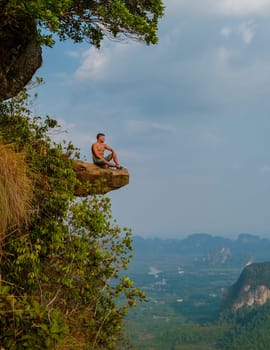 young men at the edge of a mountain, Dragon Crest Mountain Krabi Thailand, Young traveler sit on a rock that overhangs the abyss with a beautiful landscape. Dragon Crest or Khuan Sai at Khao Ngon Nak