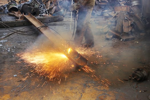 A worker recycles an old, rusty iron rail using an autogen, cutting metal with a gas torch.