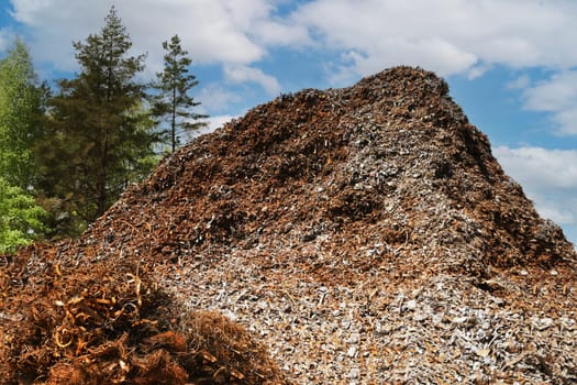 A large pile of rusty metal waste against the background of the sky and trees.