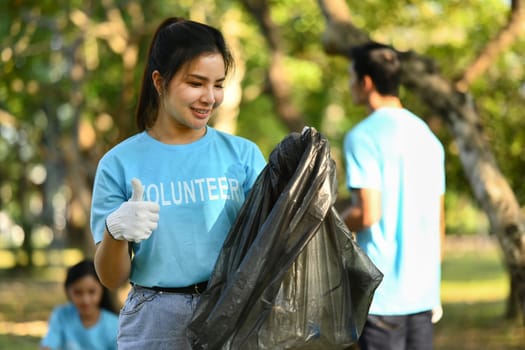 Pretty young female volunteer with garbage bags cleaning up public park. Charity and ecology concept