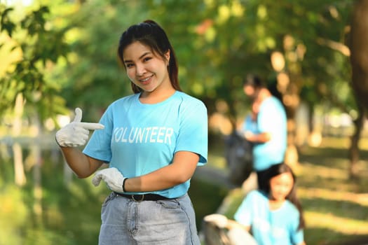 Young woman pointing to volunteer uniform while standing outdoor. Charity and community service concept