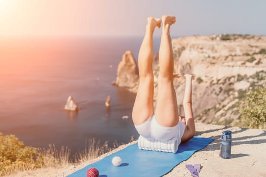 Middle aged well looking woman with black hair doing Pilates with the ring on the yoga mat near the sea on the pebble beach. Female fitness yoga concept. Healthy lifestyle, harmony and meditation.