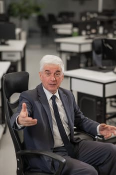 Portrait of a mature business man sitting in a chair in the office. Vertical photo