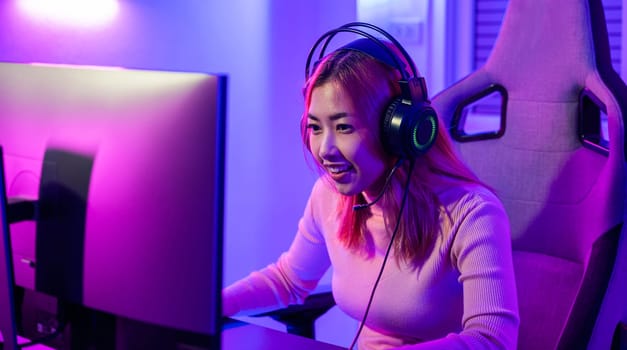 Happy Gamer endeavor plays online video games tournament with computer neon lights, young woman wearing gaming headphones intend to do playing live stream games online at home